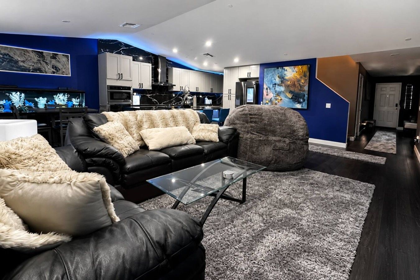 Un salon moderne avec un canapé en cuir noir, une table basse en verre et un grand tapis à poils longs de couleur grise.