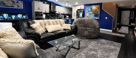 Una sala de estar moderna con un sofá de cuero negro, una mesa de centro de vidrio y una alfombra mullida gris.