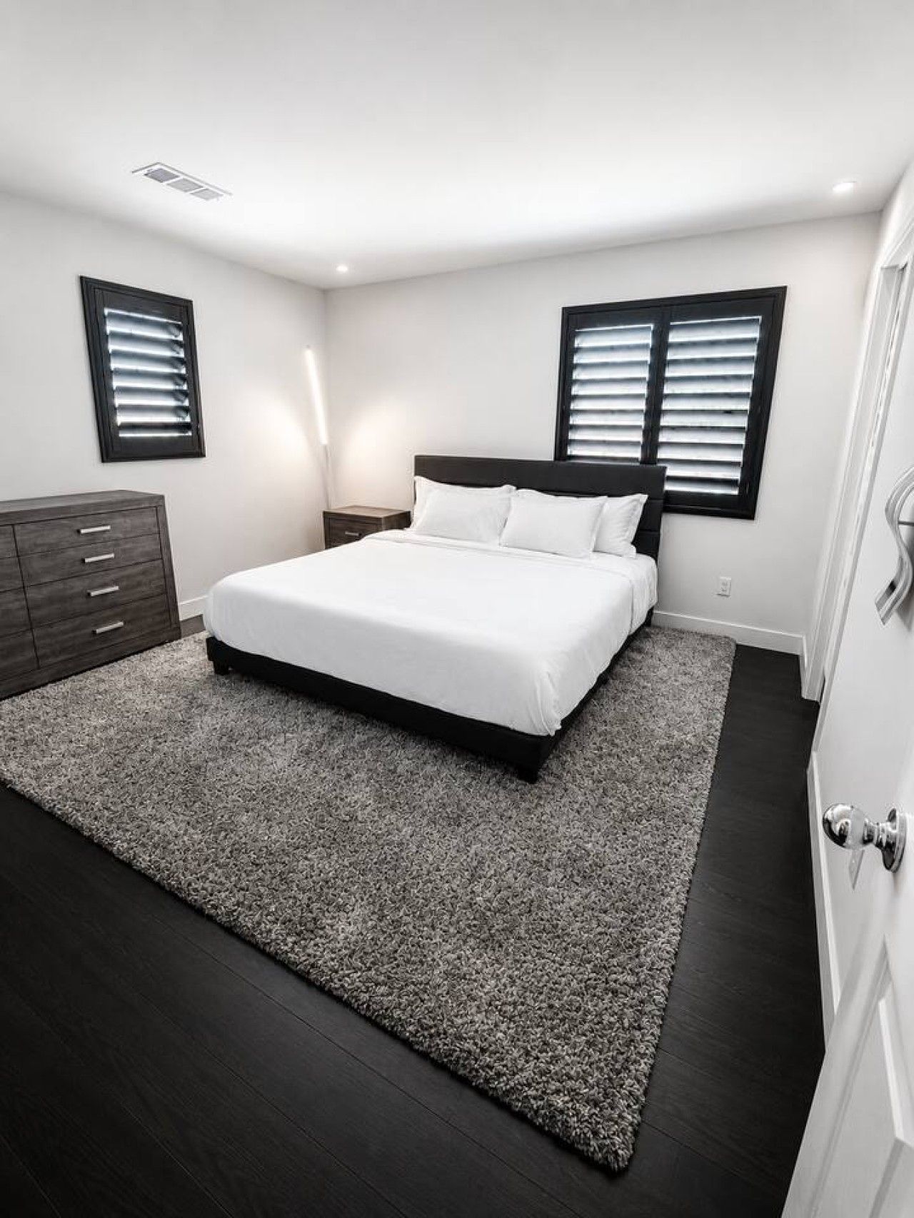 A bedroom with a bed, a dresser, and two windows with blinds.