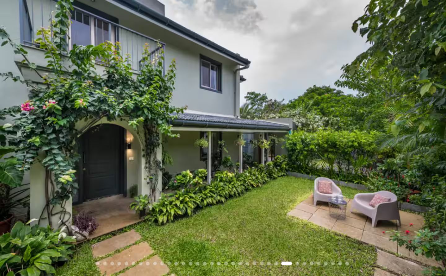 A house with a covered porch, a lawn, and two outdoor seating areas.