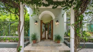 A covered entrance with a stone-paved pathway leading to a wooden door, flanked by potted plants and a metal fence. - French Villa with Private Pool (Awas)