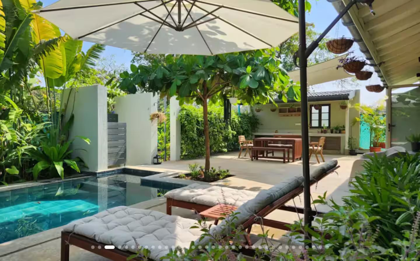 A pool area with lounge chairs and umbrellas, surrounded by lush greenery.