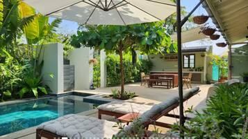 A pool area with lounge chairs and umbrellas, surrounded by lush greenery.