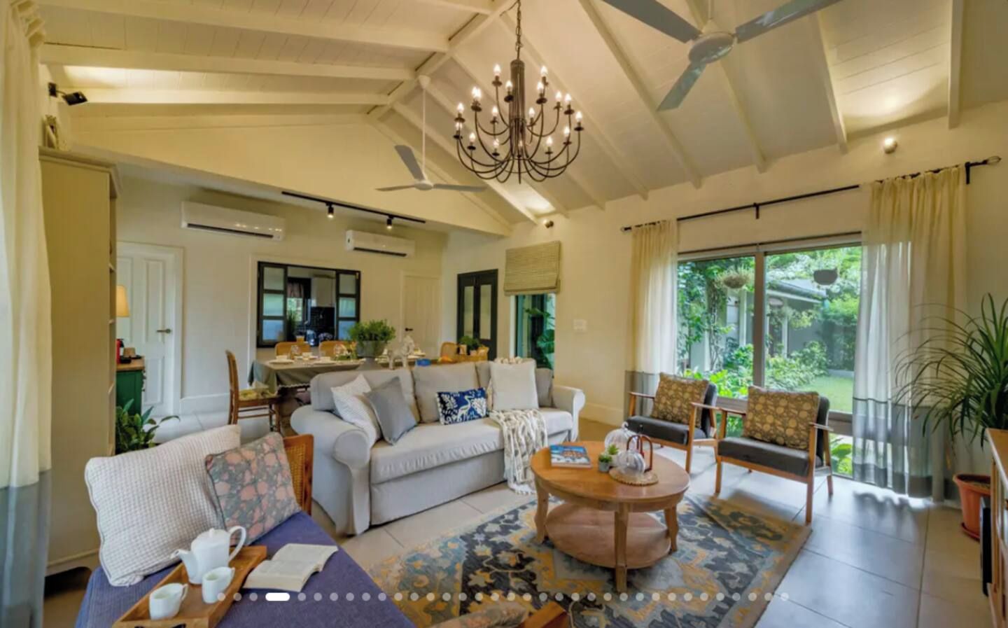A spacious living room with a chandelier, a dining area, and a view of greenery.