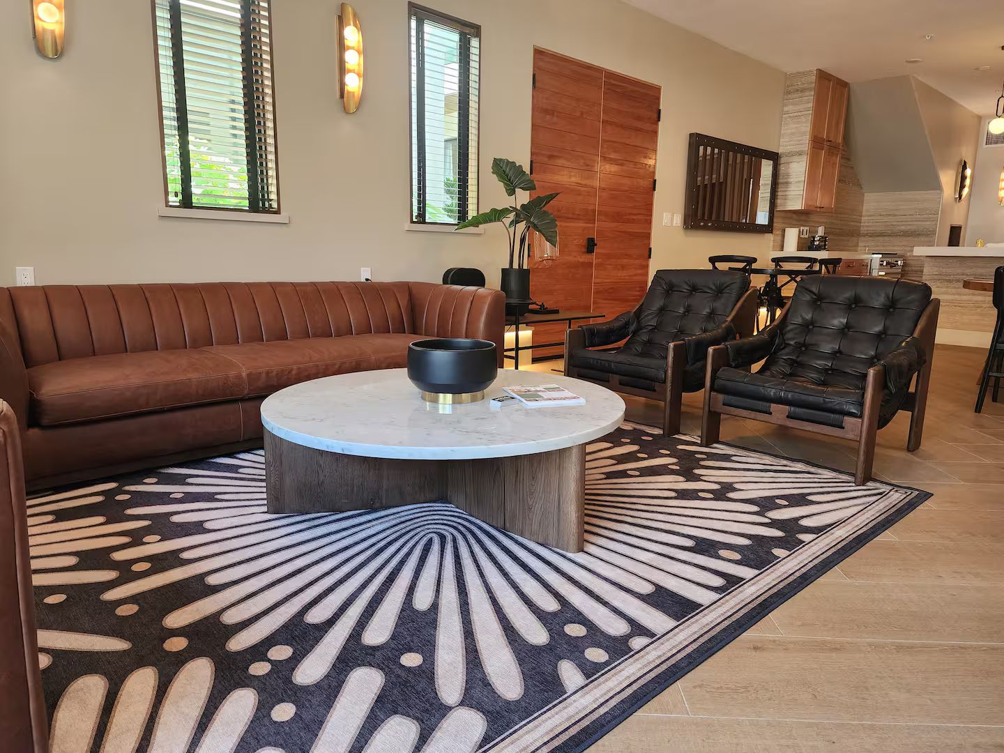Sala de estar com sofá de couro marrom, duas poltronas de couro preto, uma mesa de centro redonda e um tapete estampado.