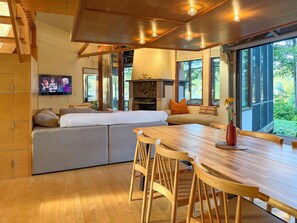 Ein modernes Wohnzimmer mit Esstisch aus Holz, bequemen Sitzmöglichkeiten, einem Fernseher und einem Kamin.