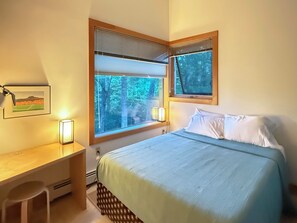 Ein Schlafzimmer mit einem Bett, einem Schreibtisch und zwei Fenstern mit Jalousien.