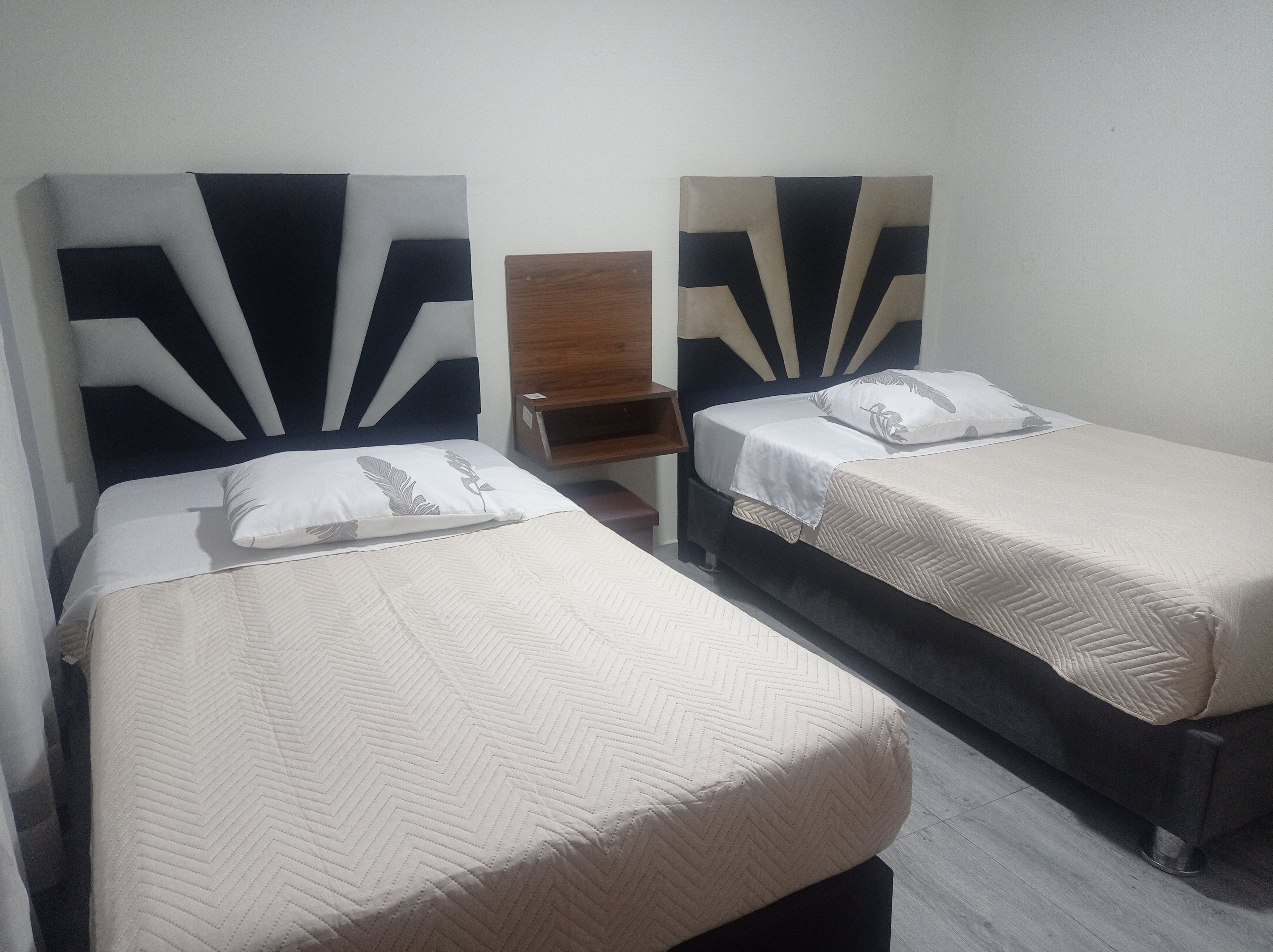 Une chambre d’hôtel avec deux lits, chacun doté d’une tête de lit au design distinct, d’une table de chevet et d’une chaise en bois.