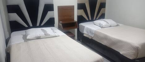 A hotel room with two beds, each with a distinct headboard design, a nightstand, and a wooden chair.