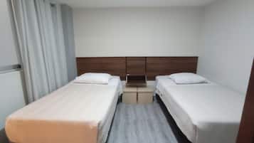 A hotel room with two single beds, a wooden headboard, a small table, and a window with curtains.