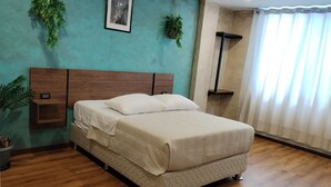 A bedroom with a bed, a nightstand, a hanging plant, a framed picture on the wall, and a window with curtains. - SAMANA INN  (Arequipa)