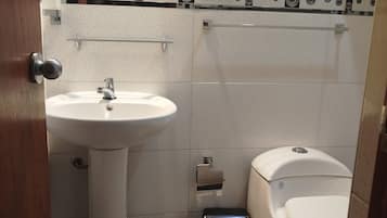 A small bathroom with a pedestal sink, a toilet, and a black trash bin.