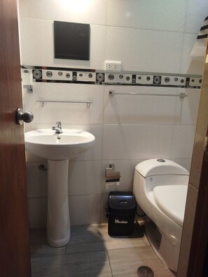 Une petite salle de bain avec un lavabo sur colonne, des toilettes et une poubelle noire.