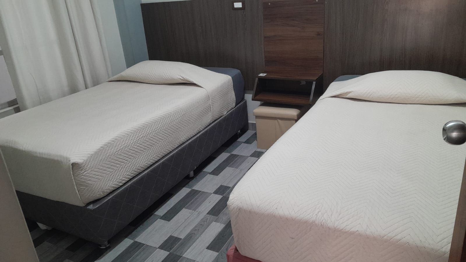 Une chambre avec deux lits, une armoire en bois et un sol carrelé.
