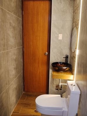 A bathroom with a wooden door, a white toilet, a sink with a bowl, and a mirror. - SAMANA INN (Arequipa)