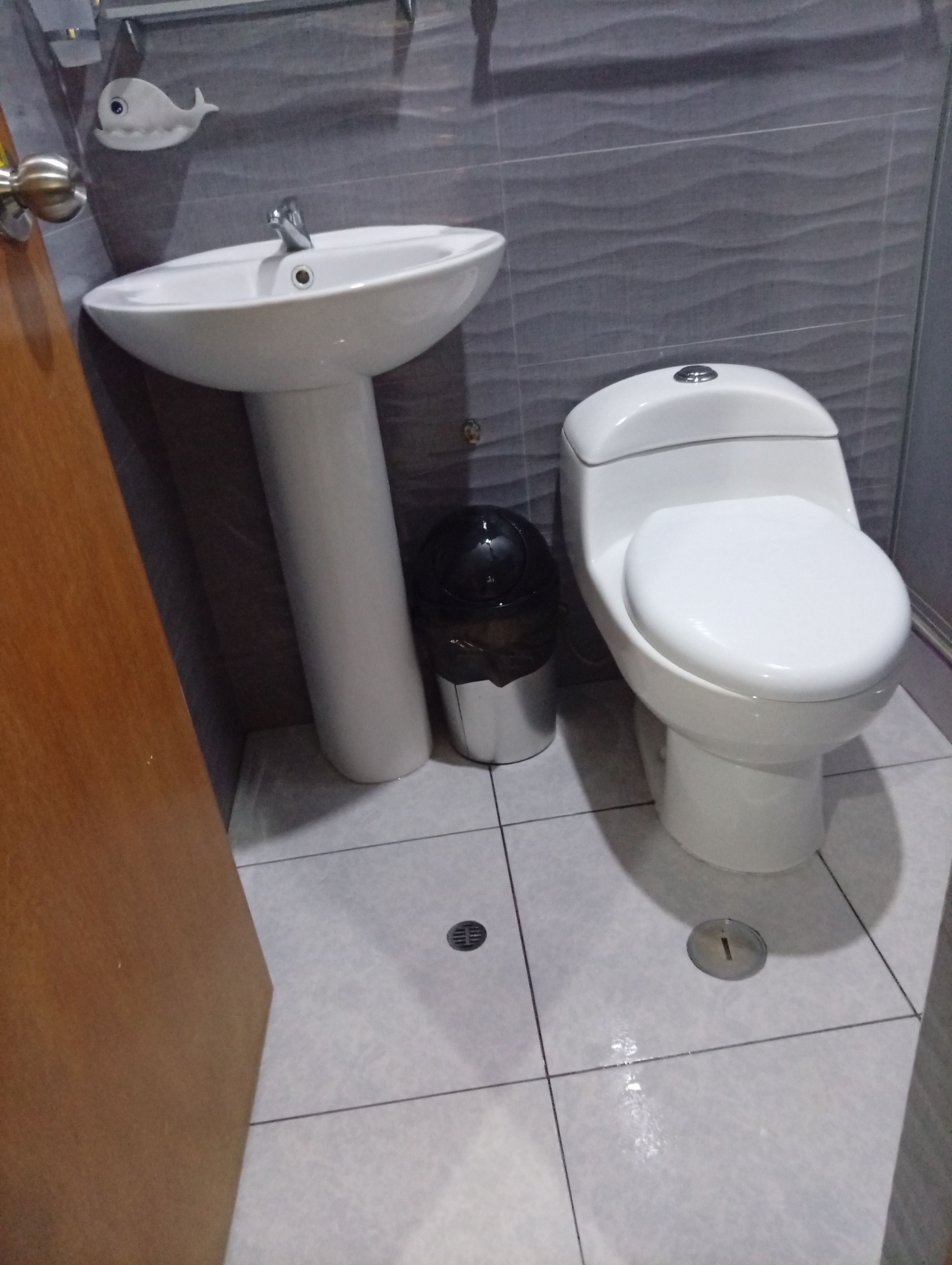 Une salle de bain avec un lavabo, des toilettes et une poubelle, le tout de couleur blanche.