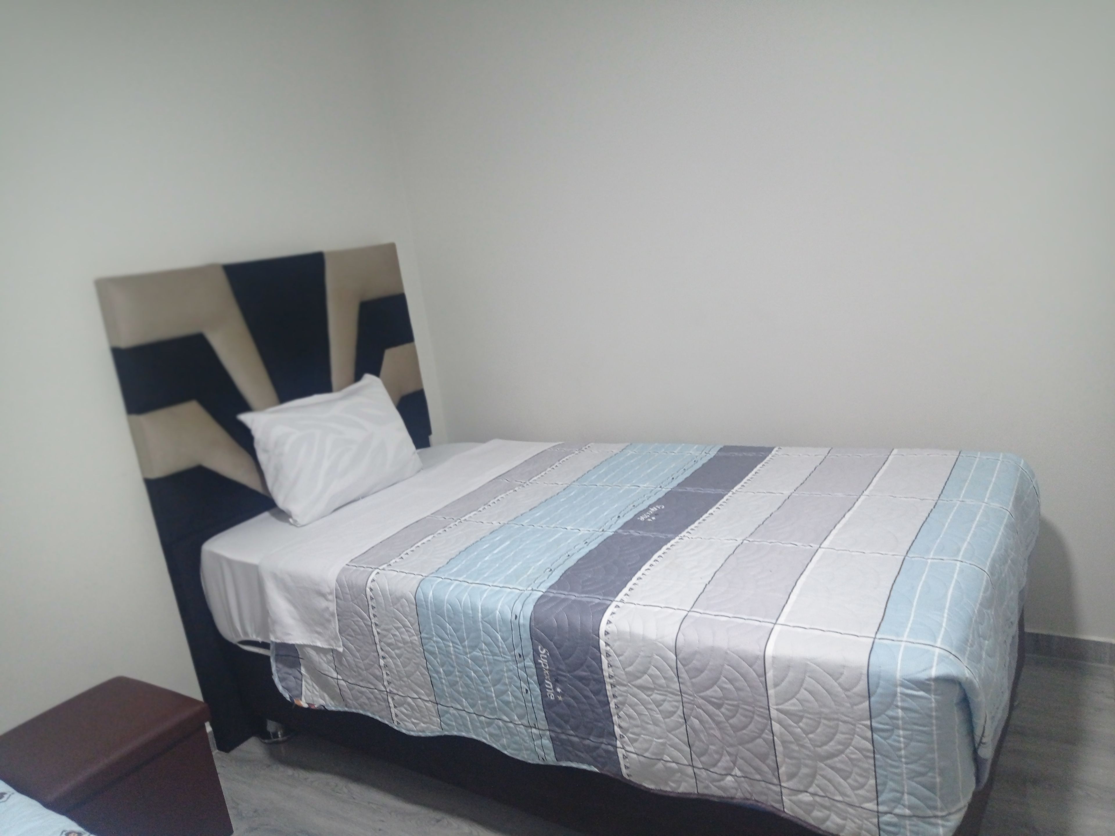A single bed with a headboard, a white pillow, and a striped bedspread.