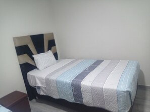 Una cama individual con cabecera, almohada blanca y edredón a rayas.