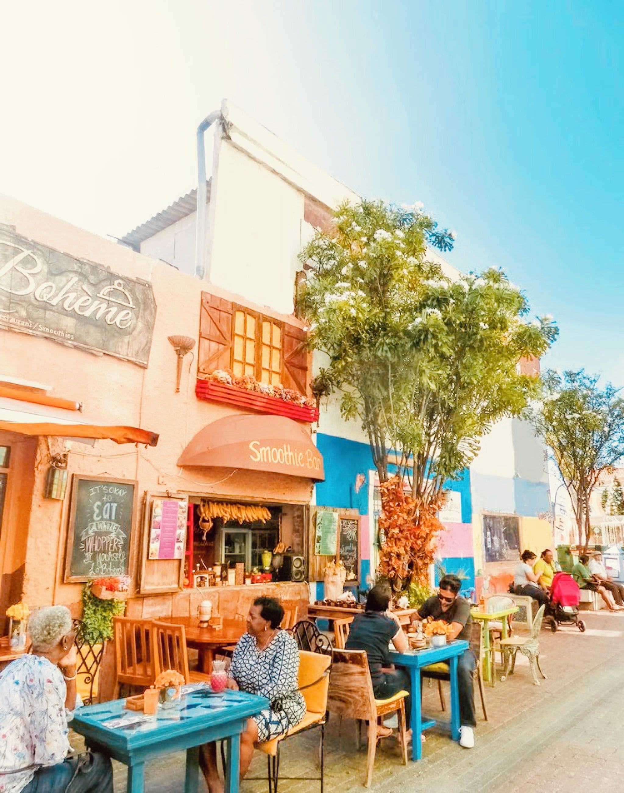 An outdoor café with tables and chairs, a sign for 'Smoothie Bar', and a building with a sign that reads 'Bohemian'.