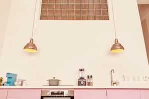 Una cocina con dos lámparas colgantes, una cafetera, una estufa y un organizador de especias.