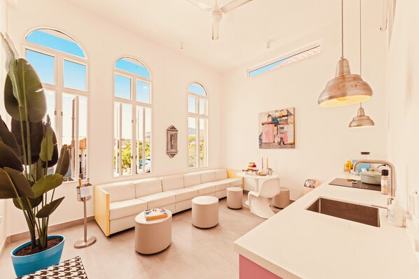 A bright, modern living room with a large window, a sofa, a dining table, and a kitchen area. - BIKINI (Willemstad)