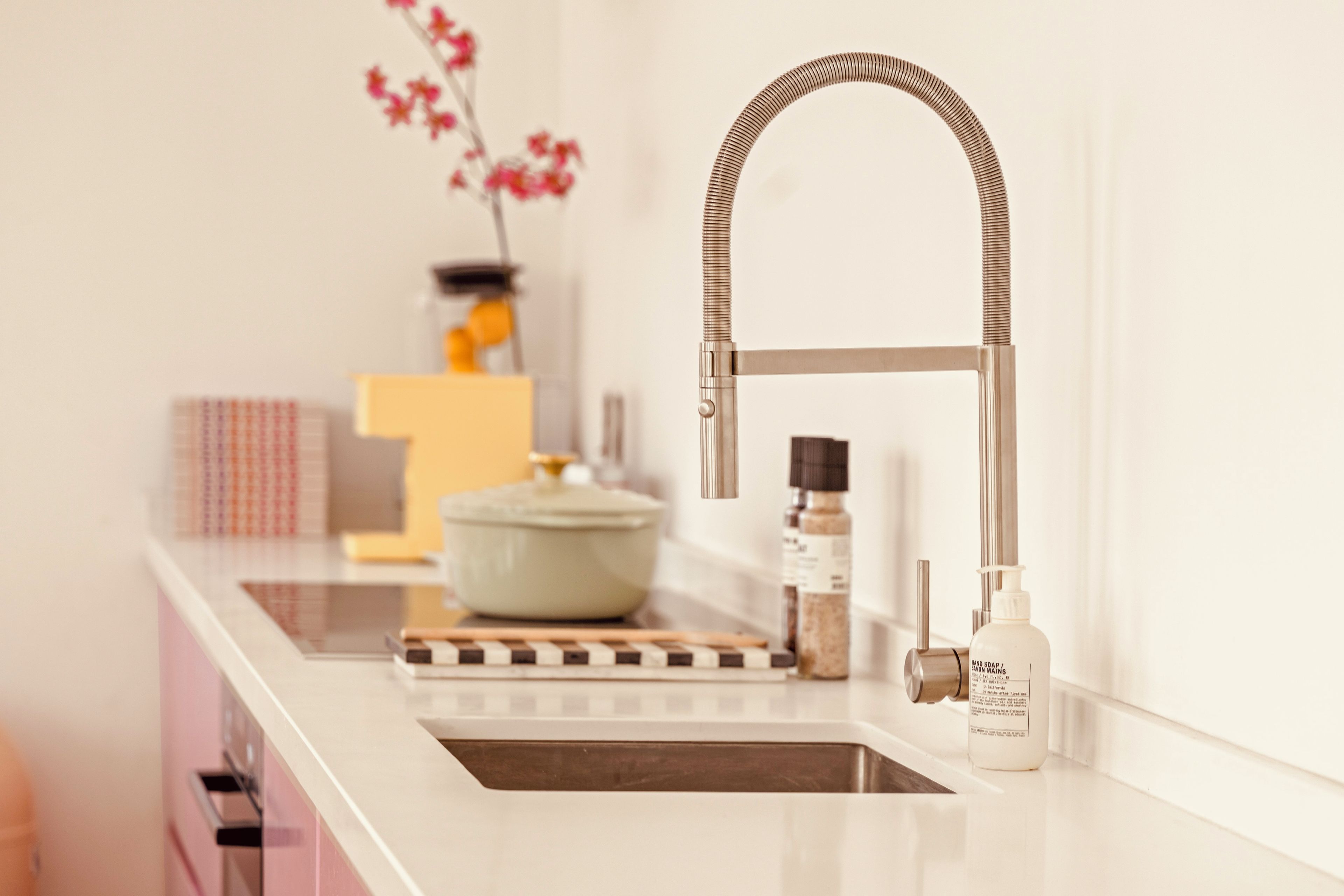 A kitchen with a modern faucet, a pot on the counter, and a bottle of hand soap.