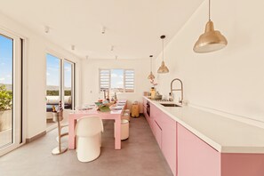 A modern kitchen with pink cabinets, a dining area with a pink table, and a view through large windows. - BIKINI (Willemstad)