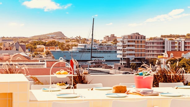 A dining area with tables set for guests, overlooking a marina with boats and buildings in the background. - BIKINI (Willemstad)