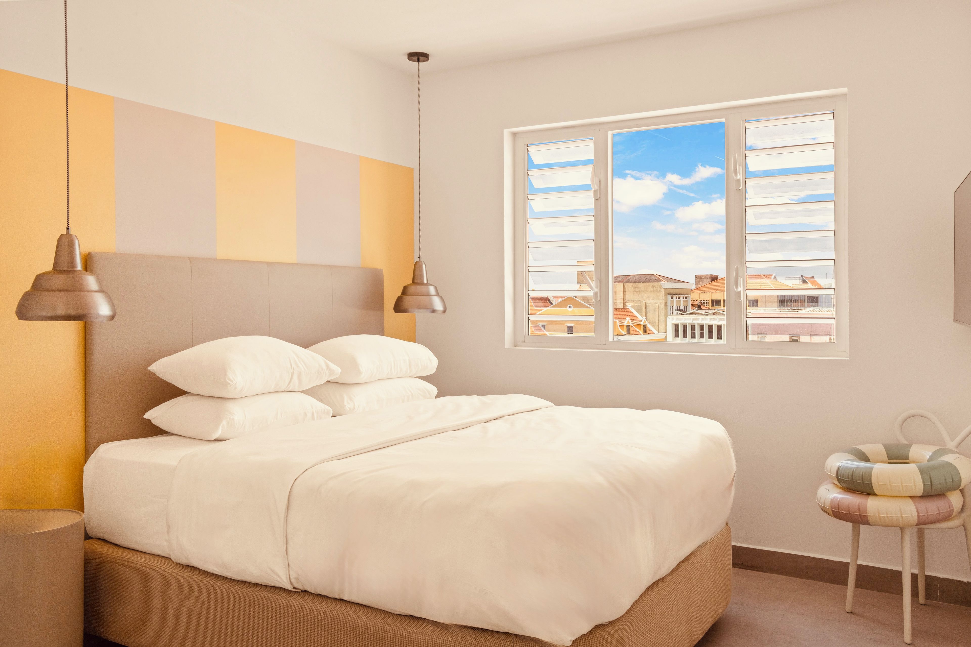 Un dormitorio con cama, almohadas, una mesita de noche, una lámpara, una ventana con vistas y una silla.