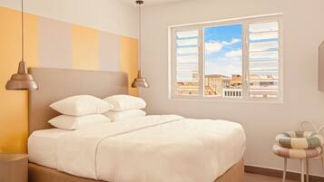 Un dormitorio con cama, almohadas, una mesita de noche, una lámpara, una ventana con vistas y una silla.