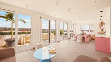 A spacious living area with a large sliding glass door leading to a balcony, a round blue table, and a kitchen area with a pink countertop.