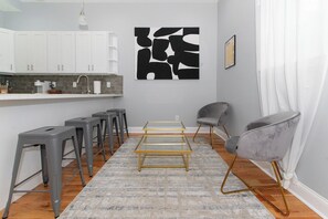 Una cocina moderna con armarios blancos, una zona con taburetes de bar y una mesa de centro de vidrio.