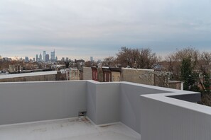Une terrasse offrant une vue sur les toits d’une ville, avec plusieurs immeubles de grande hauteur.