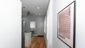A hallway with a wooden floor, a ceiling fan, a white door, and a framed artwork on the wall. - Modern 2BR 2BA Apt - Near Temple University (Philadelphia)