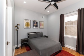 A bedroom with a bed, a standing lamp, and three framed posters on the wall.