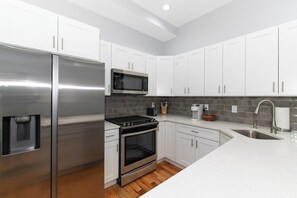 A modern kitchen with white cabinets, stainless steel appliances, a microwave, and a sink.