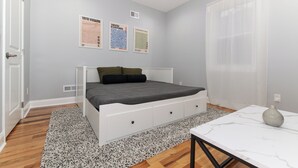 Een slaapkamer met een bed, een wit nachtkastje, een marmeren tafel en drie posters aan de muur.