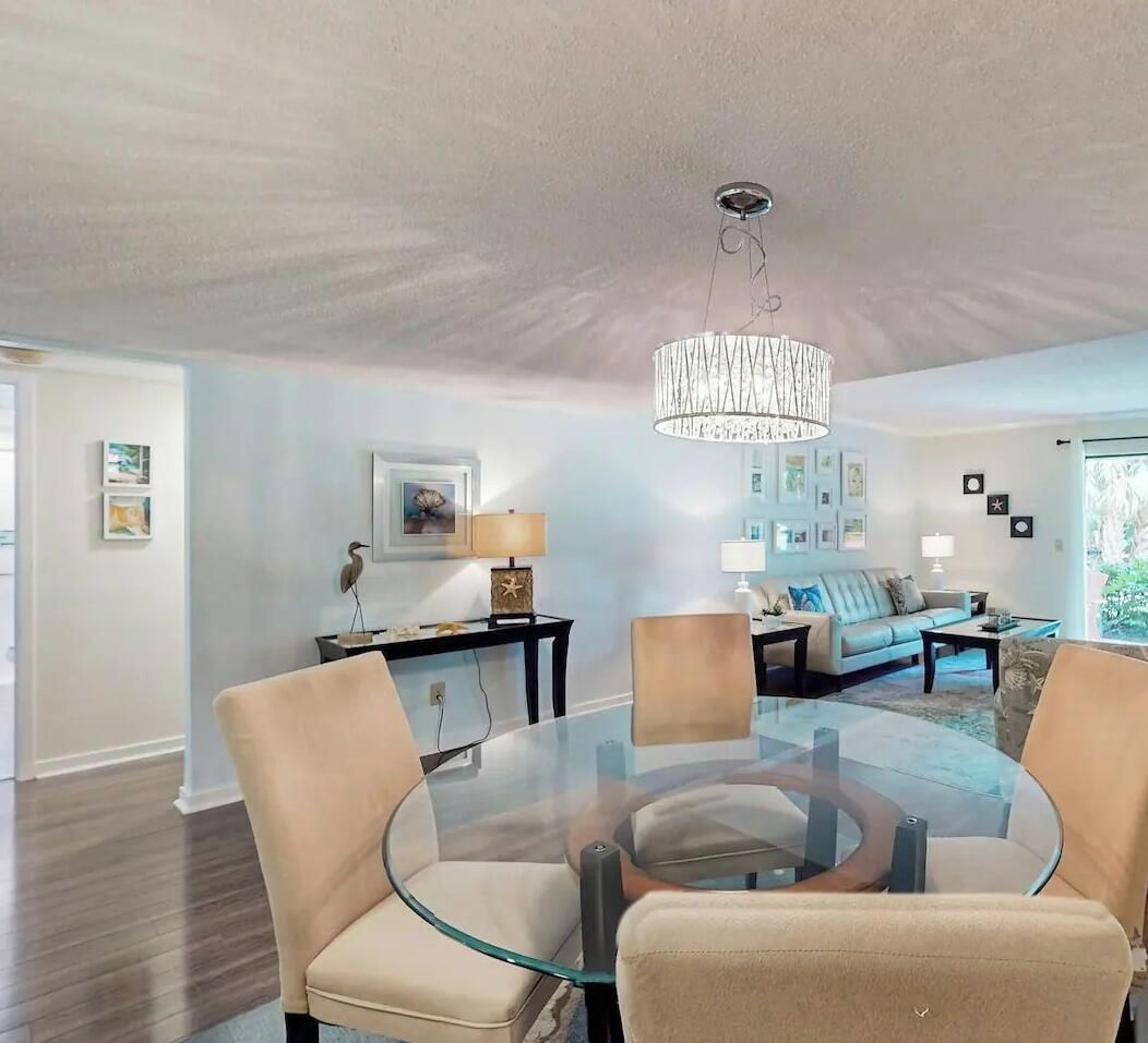 A modern living room with a glass dining table, beige chairs, a sofa, and a chandelier.