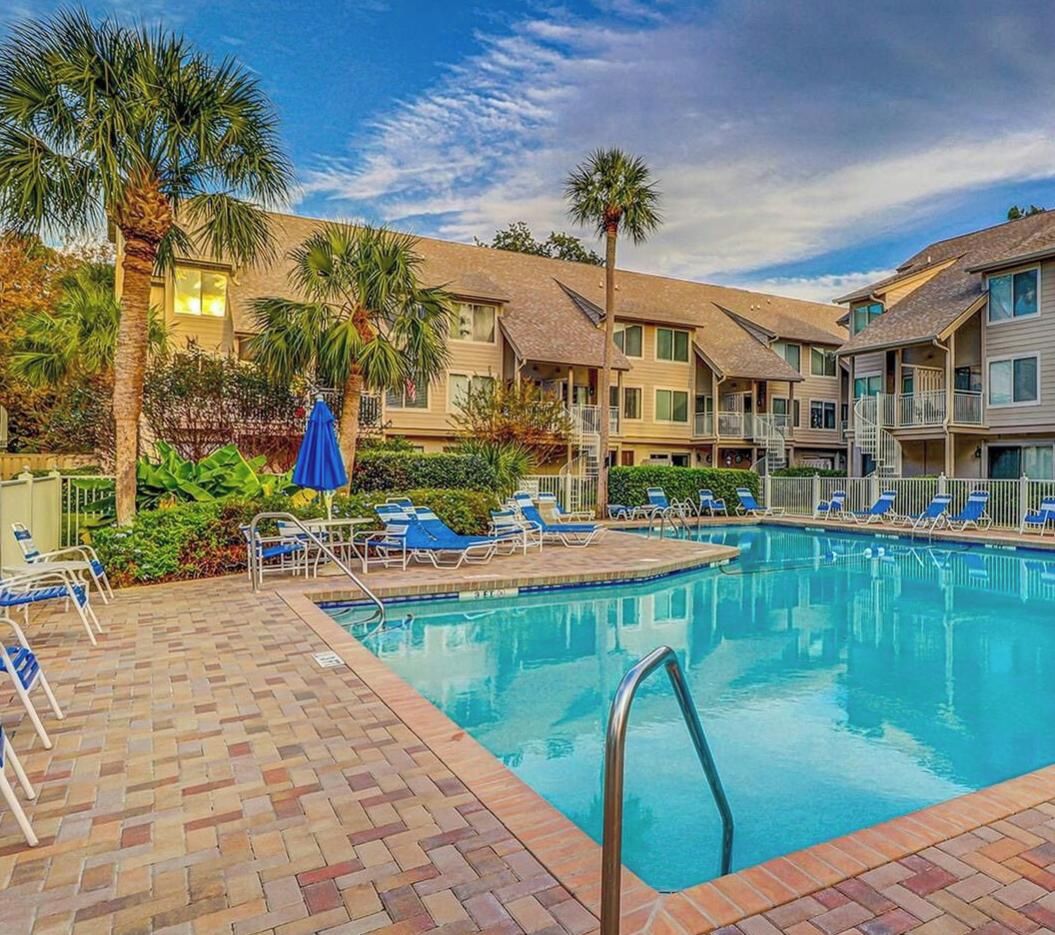 A swimming pool with lounge chairs and umbrellas, surrounded by multi-story buildings with balconies.
