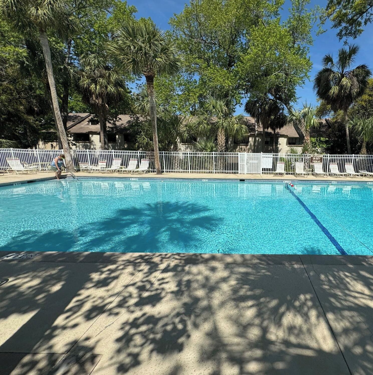Une piscine aux eaux cristallines, entourée de palmiers et bordée d’une clôture blanche.