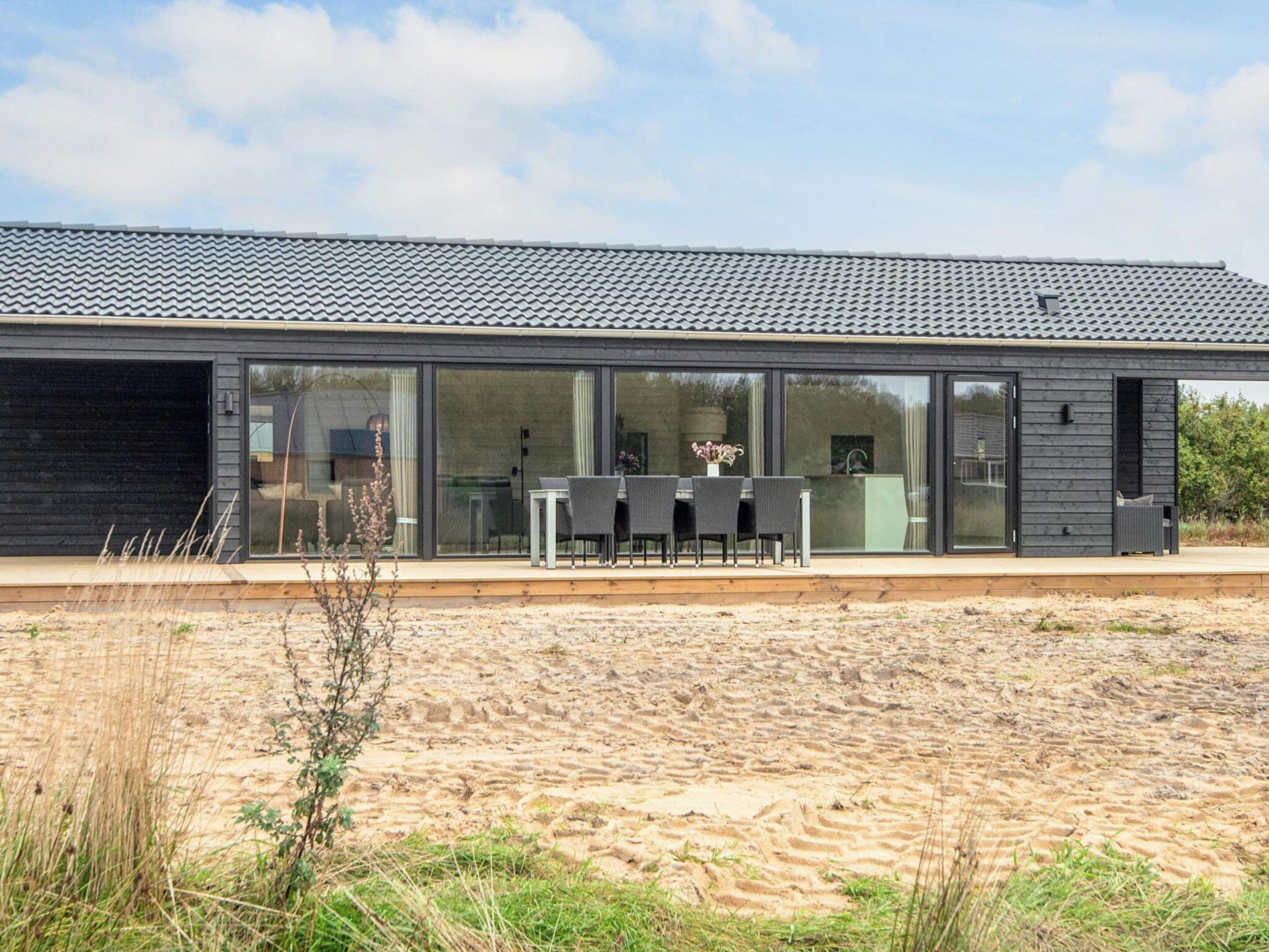 A modern house with a flat roof, large glass windows, and a patio with outdoor furniture.