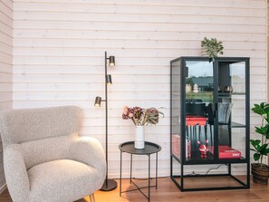 A modern room with a grey armchair, a floor lamp, a small round table with a vase of flowers, and a glass display cabinet with books and decorative items. - 5 Star Holiday Home in Romo (Rømø)