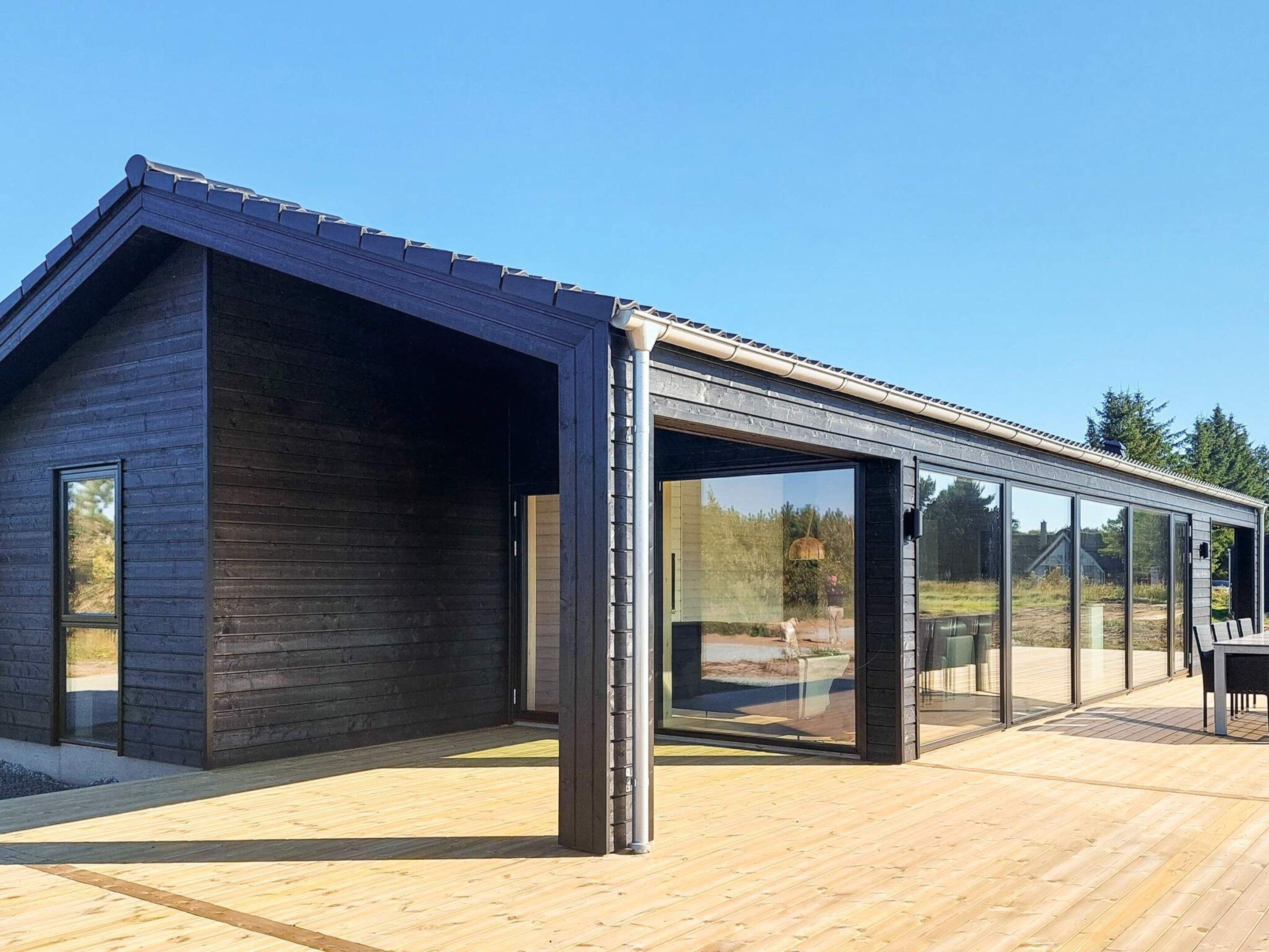 Edifici modern amb terrassa de fusta, grans finestres de vidre i teulat inclinat.
