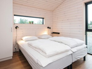 A bedroom with a wooden slat ceiling, a bed with white bedding, two wall-mounted lamps, and a window with a view of trees. - 5 Star Holiday Home in Romo (Rømø)