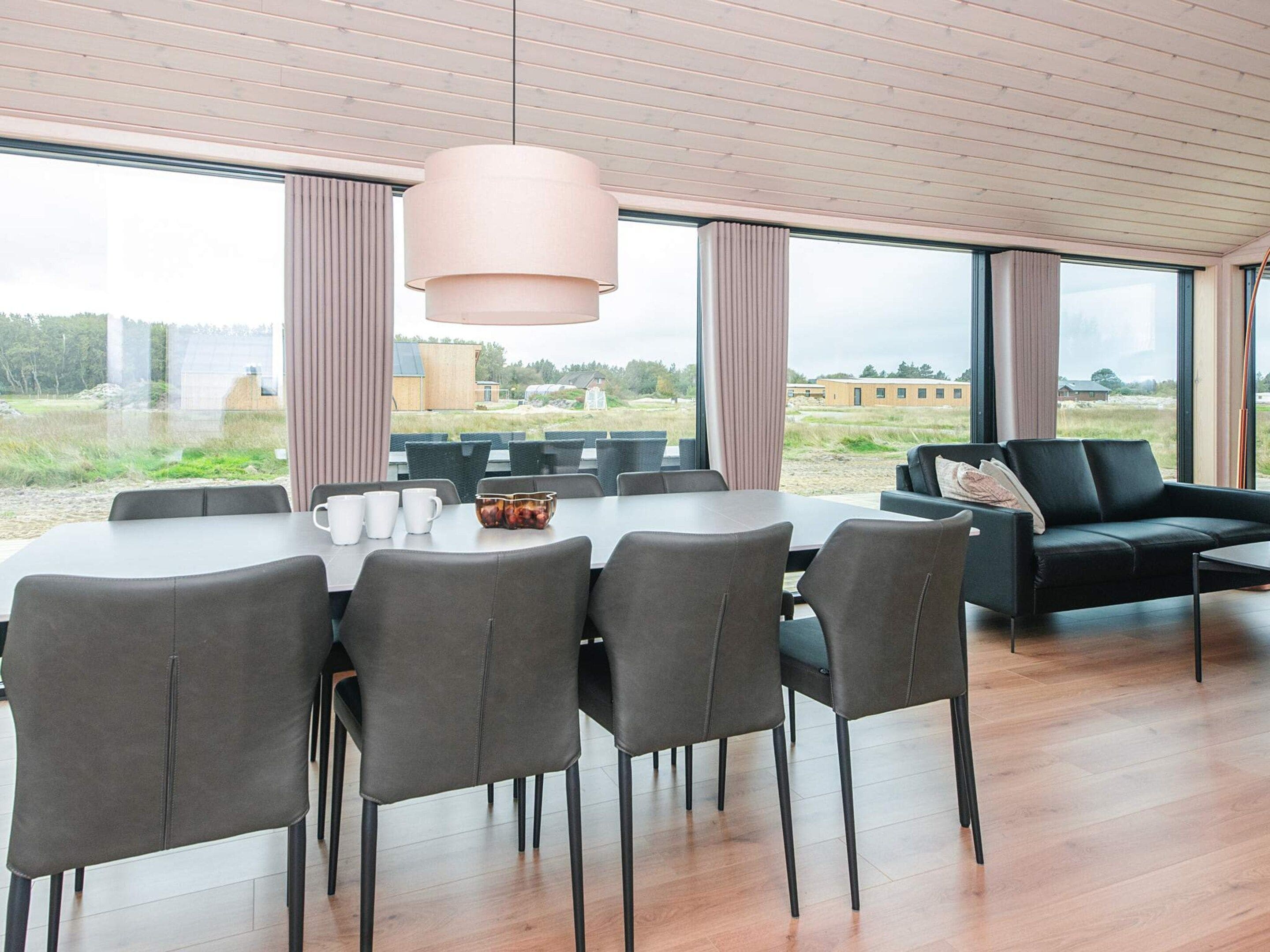 A modern dining area with a large table, chairs, and a hanging light fixture.