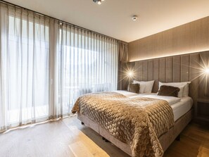 A modern bedroom with a large bed, a headboard with a starburst light, and sheer curtains. - Apartment in Schruns With Swimming Pool (Schruns)