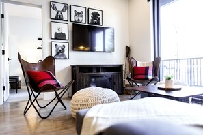 A modern living room with a fireplace, a television mounted on the wall, and a large window providing a view of the outdoors. - Monashee Sunshine (Revelstoke)