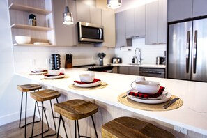 A modern kitchen with a central island, bar stools, stainless steel appliances, and a flat-screen TV. - Monashee Sunshine (Revelstoke)