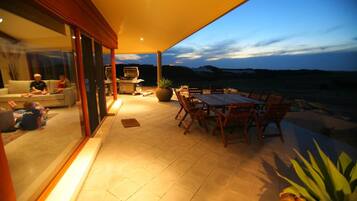 An outdoor patio with a dining table and chairs, a grill, and a view of the landscape.