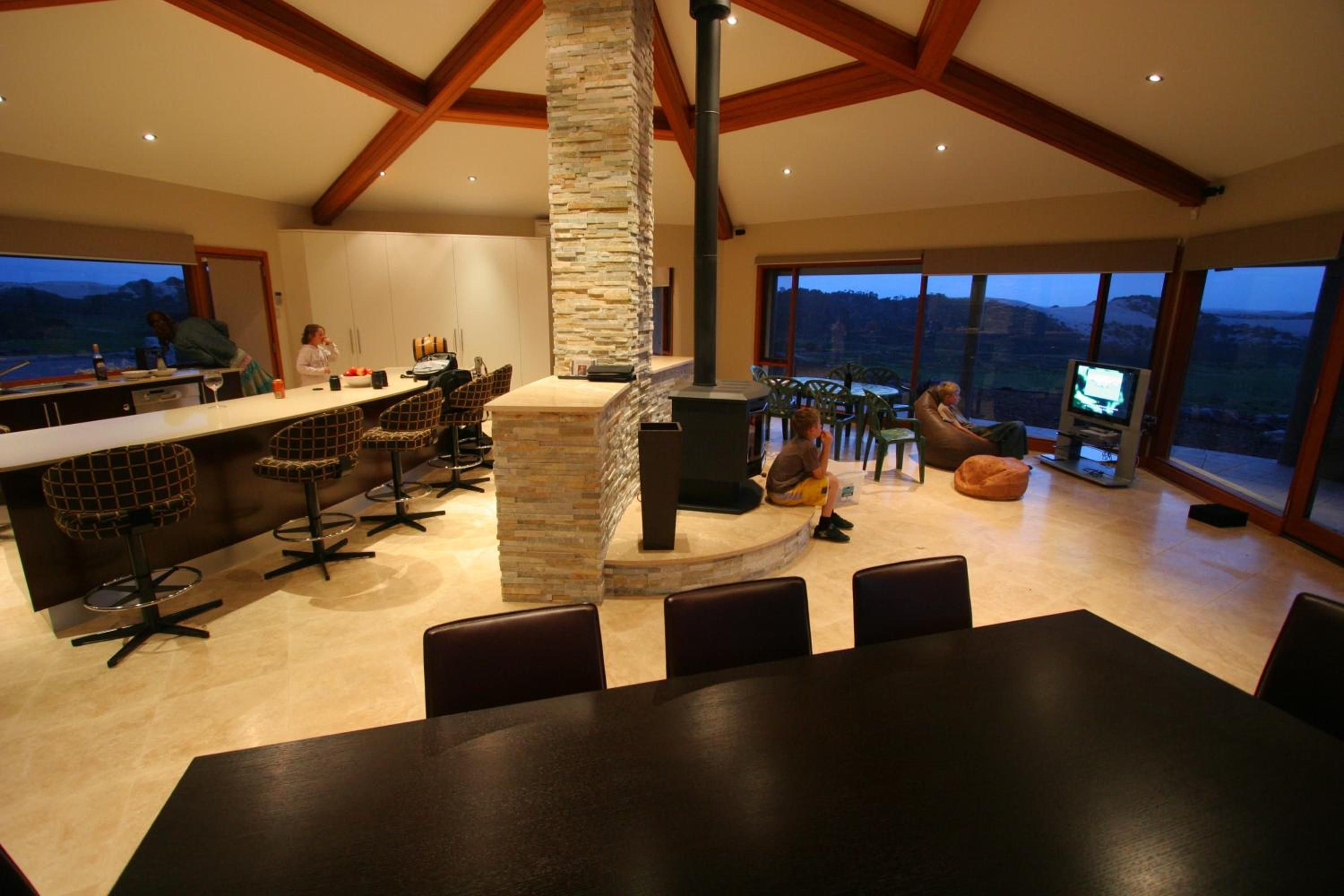 A spacious kitchen with a stone fireplace, large windows, and a high ceiling with wooden beams.